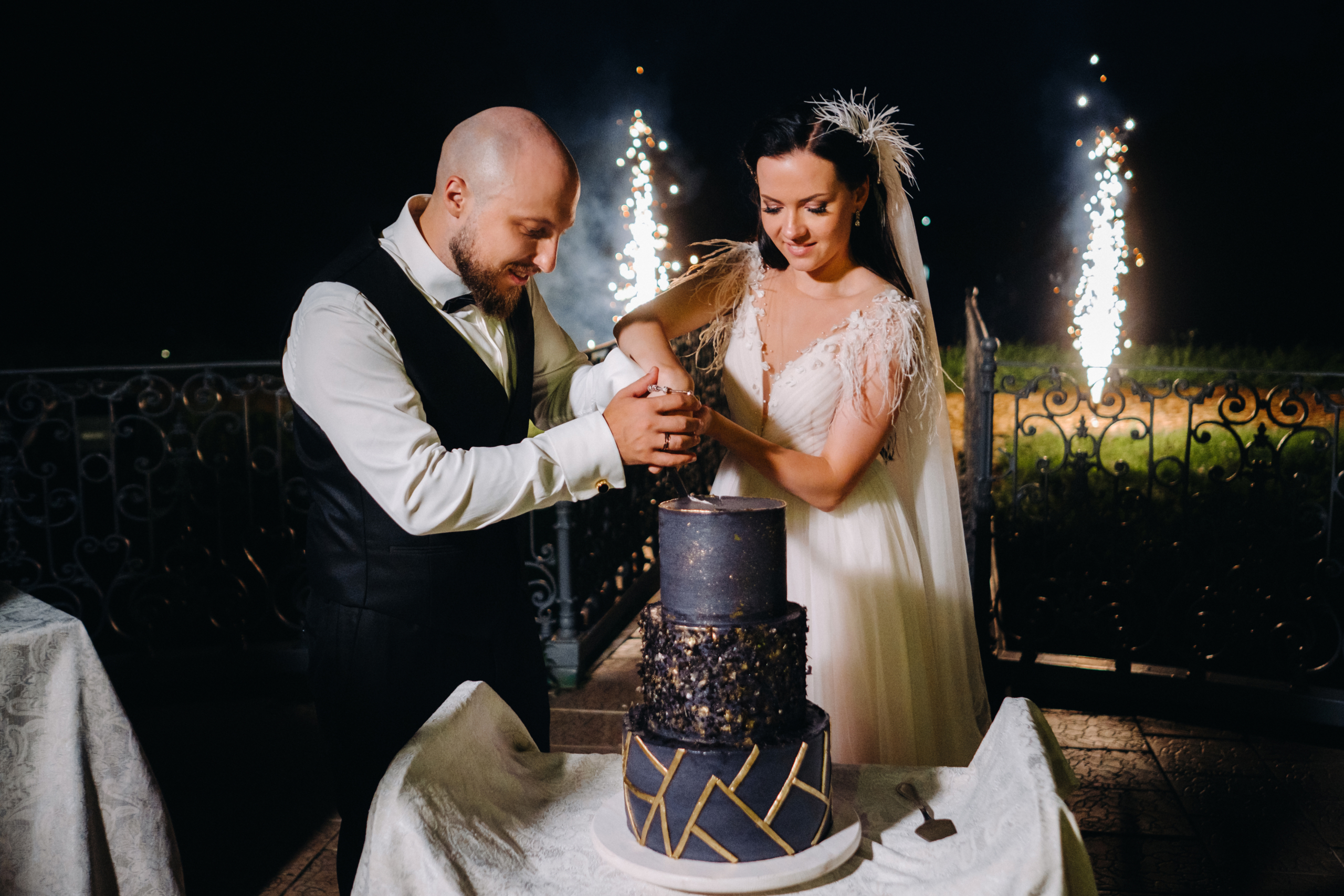 Stylish bride and groom cut the wedding cake in the evening on the street